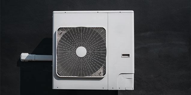 White air conditioning unit mounted on a dark wall, featuring a circular fan and sleek design.