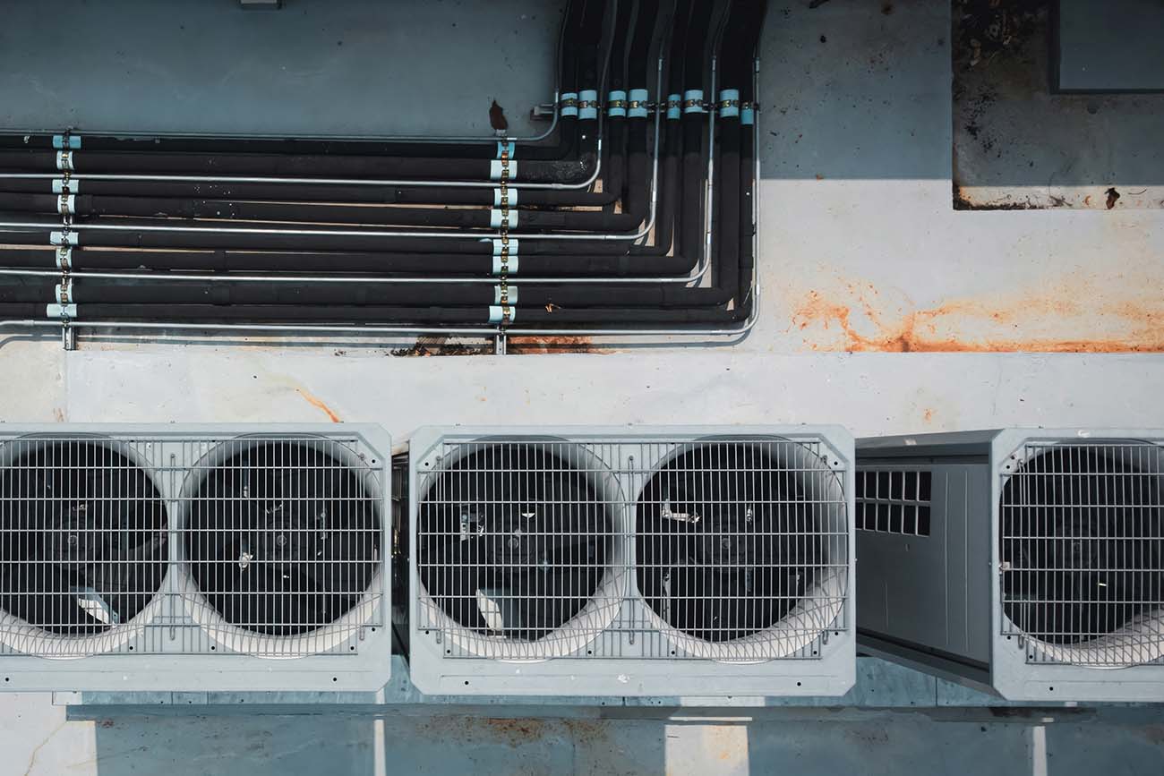 Aerial view of industrial air conditioning units and connected pipes on a rooftop, showcasing mechanical components and surface textures.