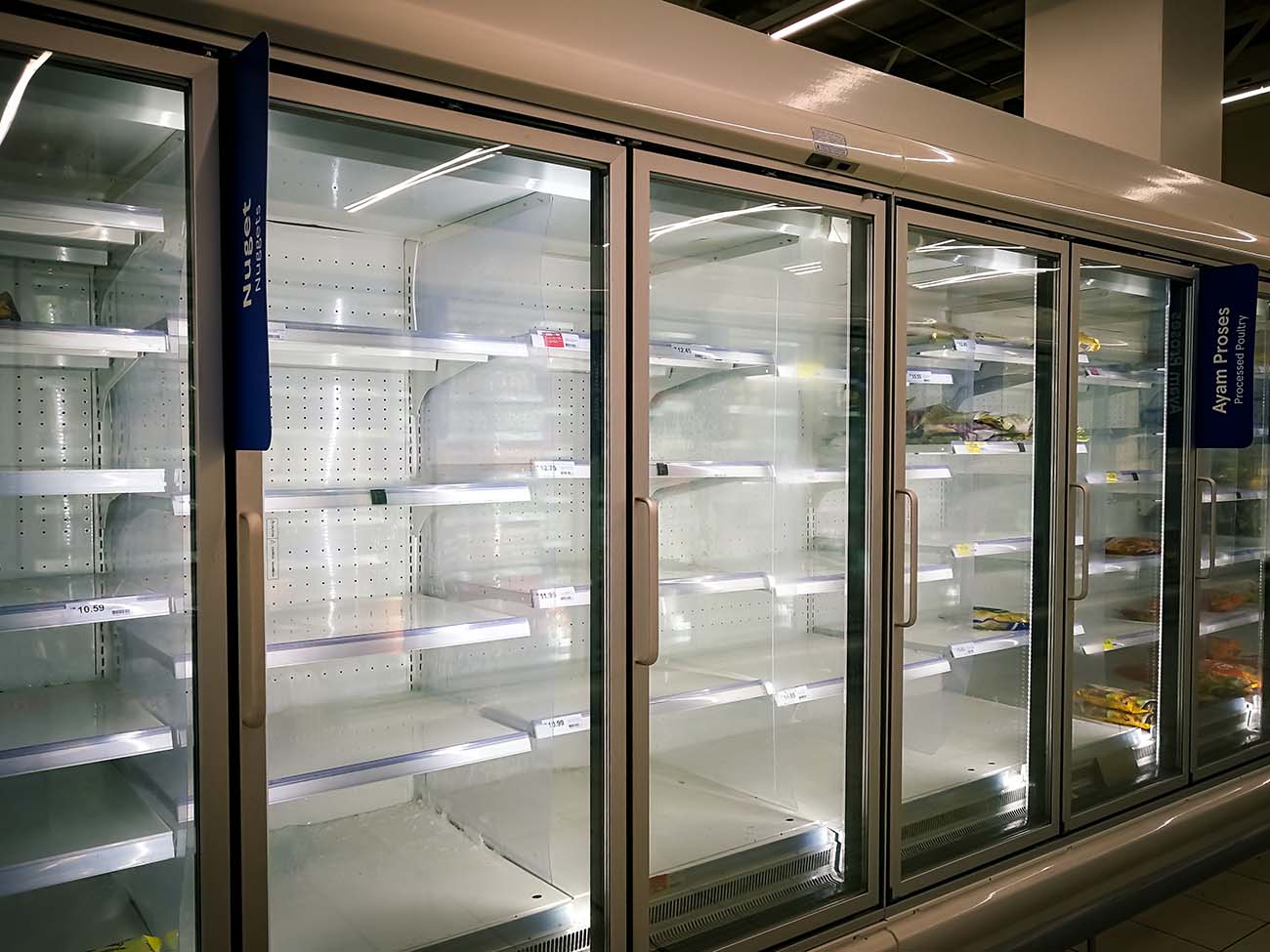 An empty supermarket freezer display with few shelves remaining, featuring labels for assorted frozen poultry products.