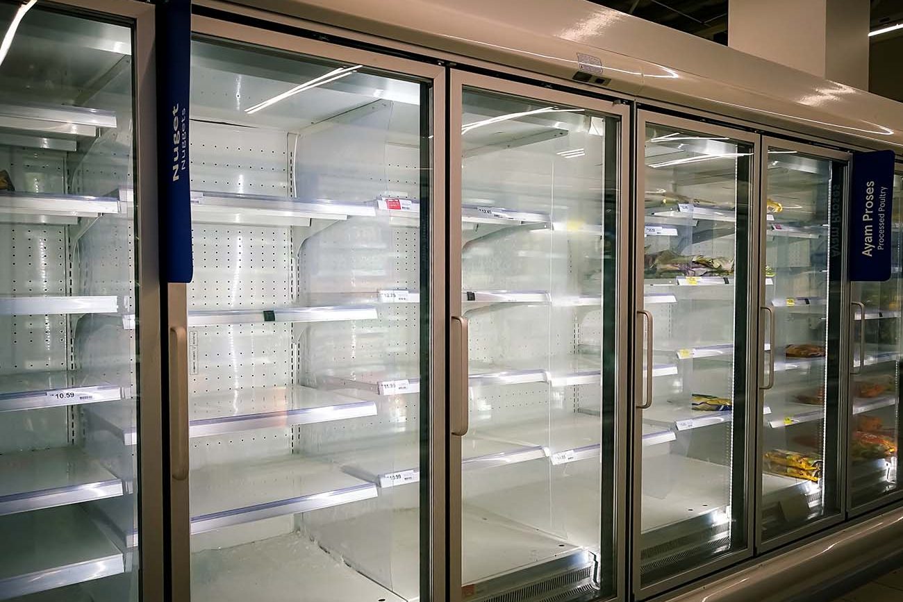 An empty supermarket freezer display with few shelves remaining, featuring labels for assorted frozen poultry products. An empty supermarket freezer display with few shelves remaining, featuring labels for assorted frozen poultry products.