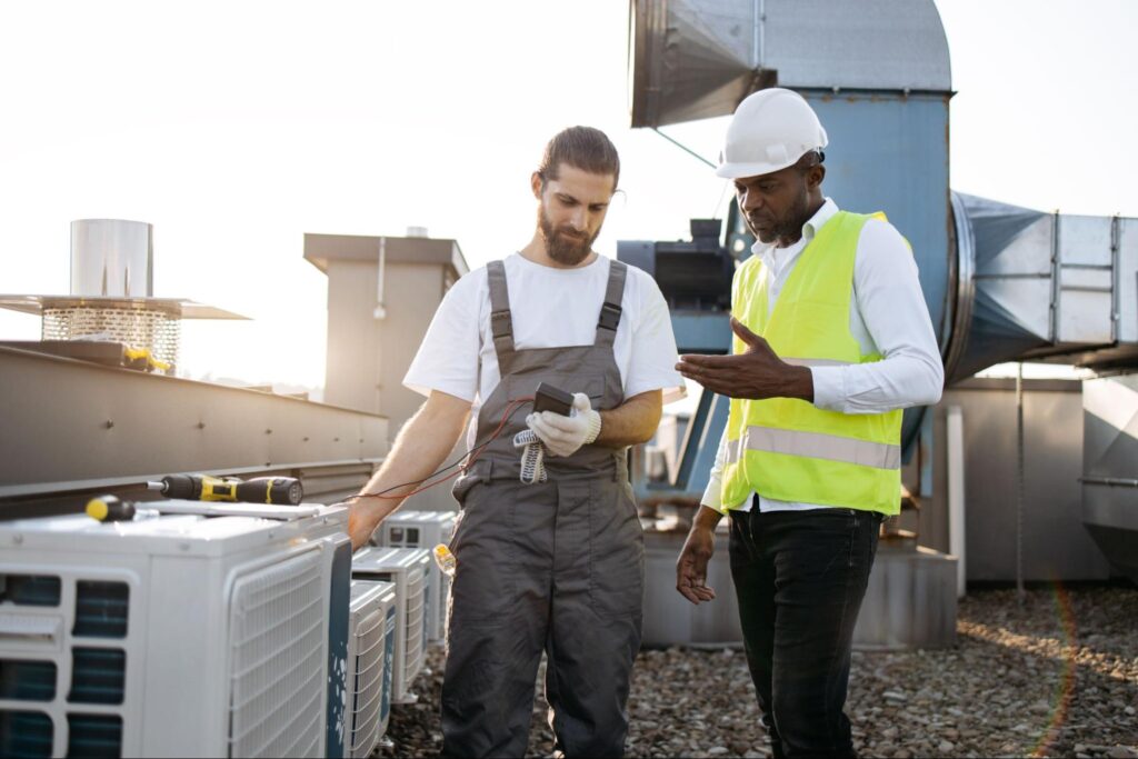 Air conditioning company workers measure the voltage on a rooftop industrial HVAC unit.