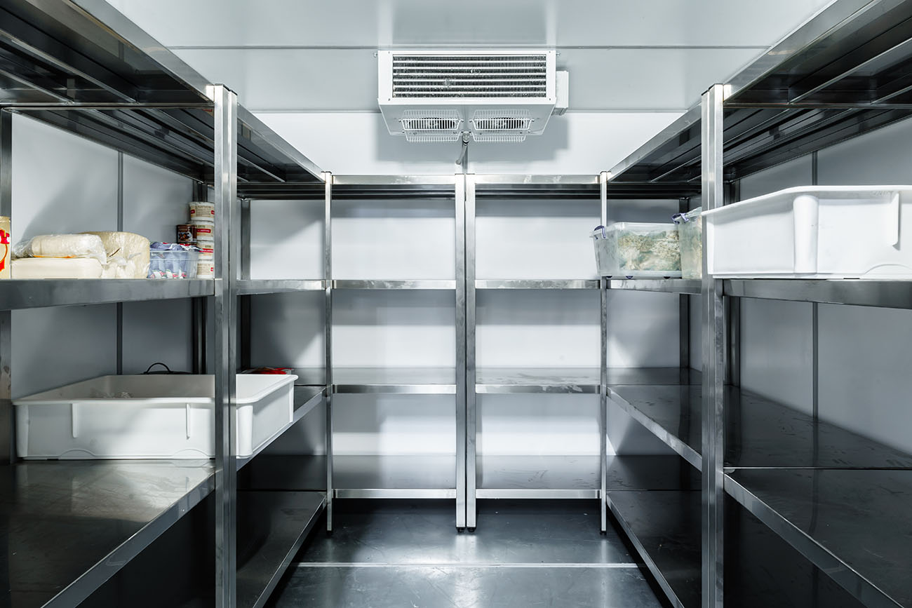 An empty commercial refrigerator with stainless steel shelves and minimal food items, featuring an overhead cooling unit.